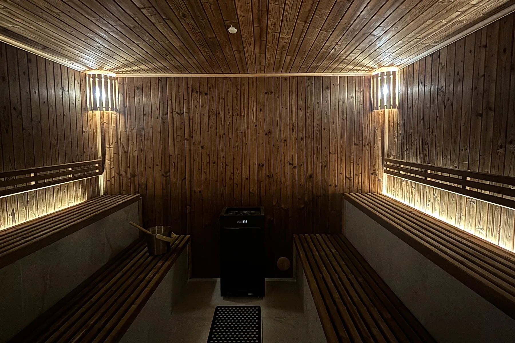 The sauna at Recovery Sanctuary: pine-clad walls and ceiling, slatted wooden benches down both sides lit from beneath by warm LED strips, the heater at the far end